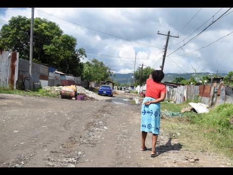 A woman walks along an unpaved road in Riverton City, western St Andrew, on Thursday. Informal settlers say they are being hounded off property they have called home for decades.