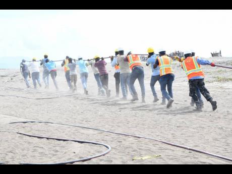 Jamaica Public Service Company workmen haul heavy electrical cables on Sunday as they race against time to have power restored to Port Royal and surrounding areas. 