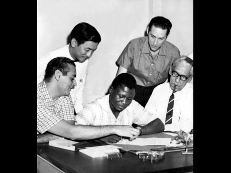 This file photo shows British Empire and Jamaica lightweight boxing champion Bunny Grant (centre) as he puts his signature on the dotted line, pointed out by his manager, Jacques Deschamps, for his fight with Doug Valliant at the National Stadium. Others (