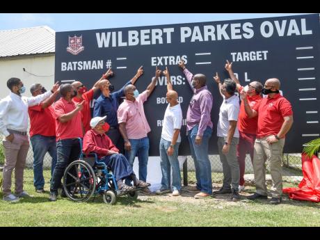 
Wilbert Parkes observes from his wheelchair as Julian Robinson (centre) and fellow Campion College past students point to the scoreboard during the unveiling of the scoreboard and dedication of the school’s cricket playing field in the former coach’s 