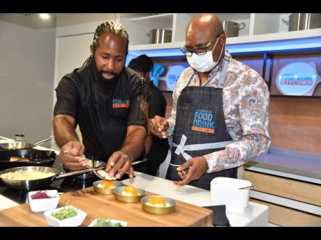 Chef Oji Jaja (left), manager of the Jamaica Food & Drink Kitchen, helps Edmund Bartlett, minister of tourism, plate a bite.