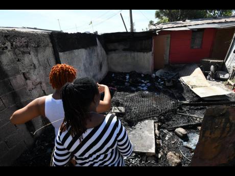 The mother (foreground) of Derran Wright surveys, along with her friend, the burnt wreckage of a home on Richie Lane on Monday. Derran Wright was shot and killed by gunmen a day earlier.
