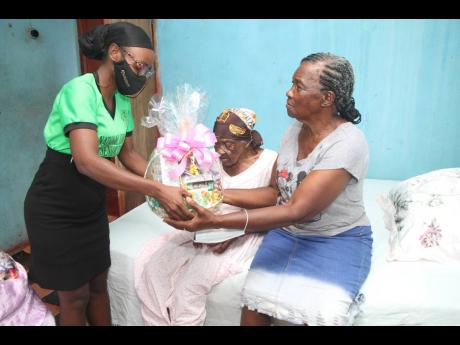 Tashane Young of the National Council for Senior Citizens, Ministry of Labour and Social Security, Clarendon, presents a basket to Louisea McDonald of Bog Hole,  the oldest person in Clarendon. 