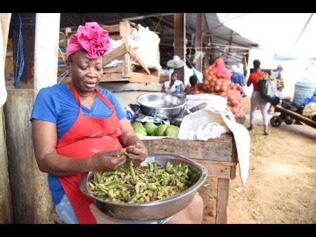 A vendor for more than two decades, Cynthia shells pods of gungo peas in the Coronation Market in downtown Kingston in hopes that sales will pick up soon.