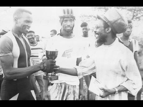 Garth Dennis (right) presents Michael McKay (left) with the first prize trophy after he had won the 'A' and 'B' Class 30-lap Cumberland Criterium cycling race. The event was sponsored by the Black Uhuru Cycling Club. A founding member of Black Uhuru, Denni