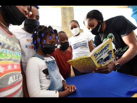 Elaine Thompson-Herah leafs through a book with children in her hometown of Banana Ground, Manchester, on Saturday during a pre-Christmas donation of care packages by The Fast Elaine Foundation. Assisting her is Tracy-Ann Jamas (second right), customer ser