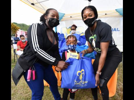 Elaine Thompson-Herah (right) presents a care package to Eneth Wallker and her five-year-old niece Jayanna Johnson when Thompson-Herah visited Banana Ground for a community treat under the auspices of her Fast Elaine Foundation.