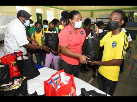 Shellyann Ebanks (centre), academic staff representative, and Kevin Nembhard (left), PTA president, hand out care package to students at the Meadowbrook High School Teacher’s Christmas Treat 2021 for 100 students and their families at the school Monday.