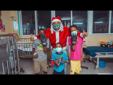 Health and Wellness Minister Dr Christopher Tufton, playing Santa Claus, shares a moment with three of the children admitted on the paediatric ward of the Savanna-la-Mar General Hospital in Westmoreland.