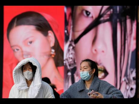 Women wearing masks walk pass ads featuring models for make-up products in Beijing, China, on Tuesday, December 28. 
