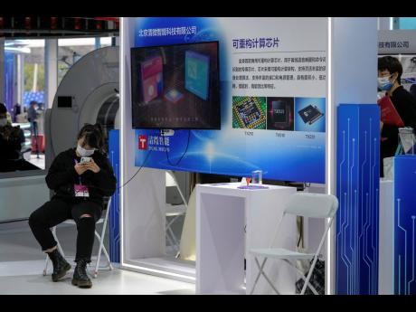 A woman wearing a face mask browses her smartphone at a booth displaying various chips developed by Beijing’s Tsing Micro at the China Beijing International High-Tech Expo in Beijing on September 26.