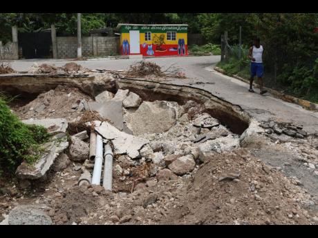A youngster walks past the collapsed road at the entrance to the Harbour Heights community in St Andrew. The roadway was devastated by rains associated with Tropical Storm Grace, which resulted in a ruptured water main.
