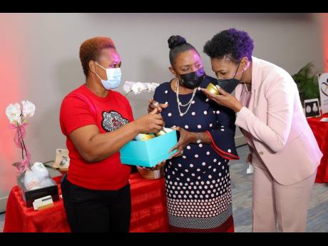 Shelli-Rai James, chief executive officer of gifting service, Straight from Yard, offers Audrey Tugwell Henry (right), president and chief executive officer, Scotia Group Jamaica, a whiff of a locally-made candle. Olivia ‘Babsy’ Grange, minister of cul