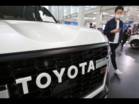 A man walks by the logo on a Toyota car at a showroom in Tokyo in 2021. The shortage of parts caused by the coronavirus pandemic is further denting production at Toyota, Japan’s top automaker. 