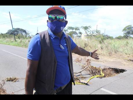 Frederick Bryan, president of the Vere Taxi Association, Clarendon, points to a crater caused by a collapsed drain along the Lionel Town main road in the vicinity of Monymusk Glades.