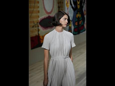 A model wears a delicate dress, in a soft beige palette, down the Dior runway. 