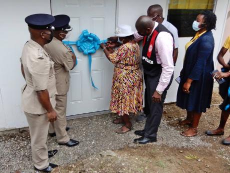Veronica Anderson cutting the ribbon to her new home, while others (from left): SSP Dwight Powell, ACP Calvin Allen, Cpl Howard Francis, Councillor Ian Bell (partially hidden), and Ferron Hayden-Coburn of the Poor Relief Department. 