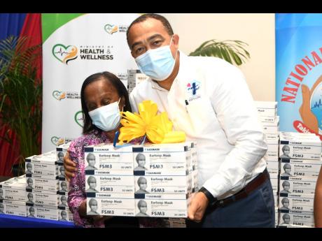 Dr Christopher Tufton, minister of health and wellness, presents masks to Gloria Goffe, executive director of the Combined Disabilities Association, at a ceremony for the handover of 2.5 million non-surgical masks to various groups by the National Health F
