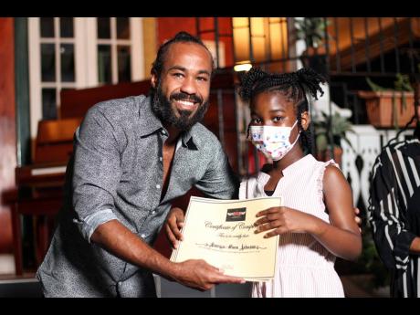 Jonathan Buchanan hands 11-year-old Kenya-Marie Johnson a certificate of completion for the beginner’s course in piano lessons, music theory and practical exercises. 
