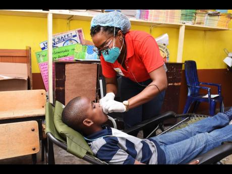 Joseph Stewart, 10-year-old May Pen Primary School student, gets a dental treatment from Dr Dominique Reid.