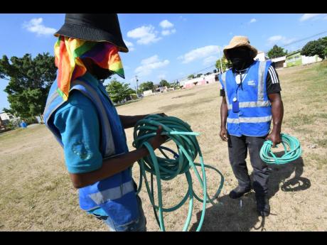 Representatives of the National Water Commission  on Windermere Avenue in Cumberland, St Catherine, where residents have connected a water hose to a fire hydrant, channelling water to a common area in the community.