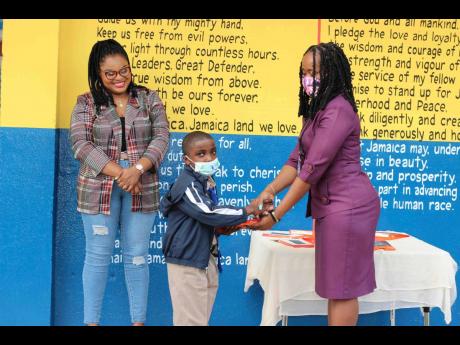 Principal of Chapelton Primary School Christine Monroe Walters (right) presents a student with a tablet while Jodian Pantry looks on.