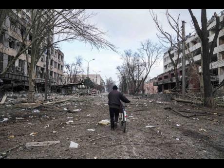 AP 
A man walks with a bicycle in a street damaged by shelling in Mariupol, Ukraine, Thursday, March 10, 2022.