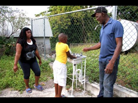 Devon-Lee Gordon assists Adjani Reid with the handwashing station erected at Red Hills Primary & Infant School while Avey Roberts looks on. 