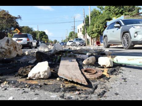 Debris litter a section of Maxfield Avenue in St Andrew yesterday as residents blocked the thoroughfare to protest the death of Emeilo Morris, who cops say was killed in an alleged shootout with them. Residents say he was murdered in cold blood.