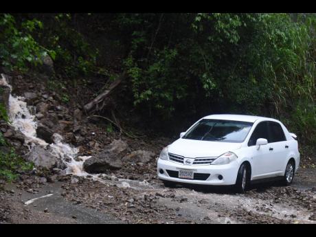 
The driver of a Nissan Tiida motor car drives past a minor land slippage along the Irish Town main road on Sunday. Storm rains affected several parishes.