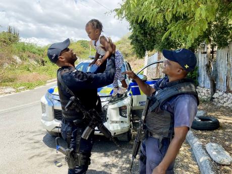 Constables Romaine Henry (left) and Renor Stewart play with one-year-old Kylie Spence in Wareika Hill, east Kingston, during their community policing efforts on Friday.