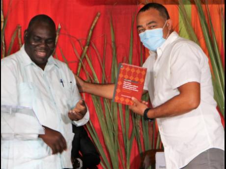 Author Dr Donovan Stanberry (left) is congratulated by Minister of Health and Wellness Dr Christopher Tufton, who accepts a copy of his book ‘How Trade Liberalization Affects a Sugar-Dependent Community in Jamaica: Global Action; Local Impact’ followin