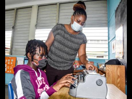 Gisellene Laing, grade six teacher at the Salvation Army School for the Blind, monitors Jhanelle Palmer as she uses one of the few Braille machines that the school had before Tuesday’s donation of 20 by the United Nations Development Programme. 