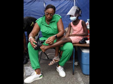 Juliet Holness, member of parliament for St Andrew East Rural, fits a shoe on the foot of a child during a medical camp sponsored by the Indian High Commission in Gordon Town on Sunday.