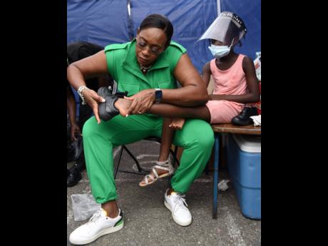 Juliet Holness, member of parliament, St Andrew East Rural assists a little girl with her shoes during a medical camp hosted by the Indian High Commission on Sunday.