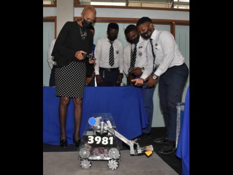 Fayval Williams (left) minister of education and youth is assisted by members of the Jamaica College Robotics team to manoeuvre their robot during a STEM career forum at the University of the West Indies (UWI), Mona Assembly Hall on Friday.