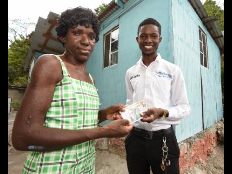 Jahzeal Clarke presents Clover Powell with some cash to help her get back on her feet shortly after the official handover of a house he built for her through his ministry. 