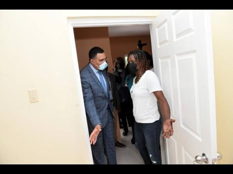 Prime Minister Andrew Holness ushers Avis Morrison into her new three-bedroom home in Greenwich Town, St Andrew, following a handover ceremony yesterday. Morrison is the beneficiary of the Government’s social housing programme.