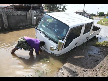 A resident of Callaloo Mews, St Andrew, affixes a chain to a disabled pickup van on a flooded road in the community after the passage of Tropical Storm Grace on Wednesday.
