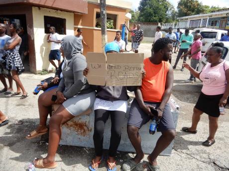 Residents, one with a placard, sit on an old refrigerator that was used to block a section of the road. 