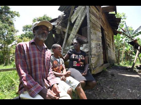 Ten-year-old Ricardo Williams is flanked by his parents, Howard Williams and Dean Edwards, outside the dilapidated structure they call home in Guy’s Hill, St Catherine. 