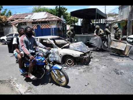 Soldiers remove burnt-out debris from a roadblock in Denham Town, west Kingston, on Monday. The community has been restive since the weekend fatal shooting of 32-year-old Horaine Glenn.