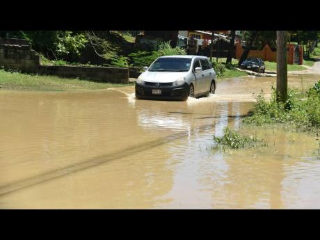 A motorist proceeds cautiously along the flooded East Avenue in Linstead, St Catherine, on Wednesday. A pond in the vicinity overflowed on Tuesday night after torrential rains, creating a headache for residents and commuters.