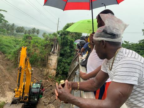 Onlookers watch as an excavator clears a section of the Montego River in St James as part of efforts to find the body of Beryl Walters on Sunday. The search for the 68-year-old will resume today.