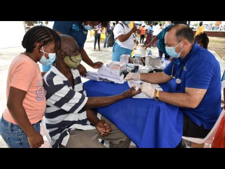 Shantwana Brown watches closely as her grandfather, Edward Shirley, gets his blood sugar checked by Nurse Miguel Etenza at the Desmond McKenzie Wellness Day of Care, put on for the homeless and Elderly and held at the St William Grant Park in Kingston on S