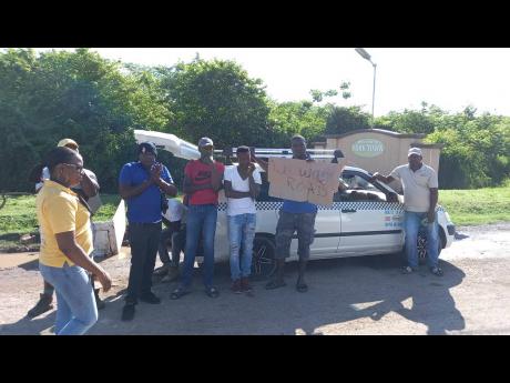A woman walks past protesting taxi drivers and residents in York Town, Clarendon, yesterday. A section of the roadway was also blocked, leaving many commuters stranded for hours.