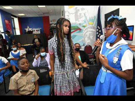 Marley Dias (centre), of the #1000BlackGirlBooks movement, listens as Courtney Greaves, student of Jessie Ripoll Primary, speaks at the GrassROOTS Community Foundation and Book Industry Association of Jamaica Education Week Book Bag outreach at the United 