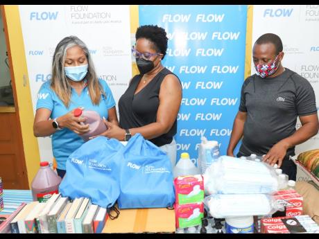 Phadra Saunders (left), director, people business partner at Flow; and Francine Rhoomes, CPFSA southern regional director, examine one of the food items donated to the Summerfield Child Care Facility during a recent visit by a Flow team, while Marlon Robin