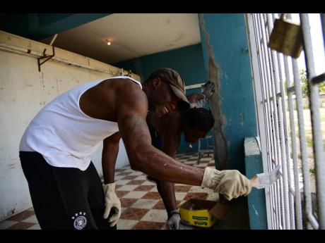 
Coach Wayne Sharpe of the G.C. Foster College Gym and Calvin Mignott (right) paint the grilles at the Olympic Gardens Football Club building which houses Suga Knockout Boxing Gym on May 7, 2022.
