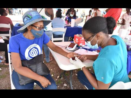 Morene Clarke (left), president of the Optimist Club, gets her blood pressure checked by Deborah Dawes, health technician at The Diabetes Association of Jamaica.